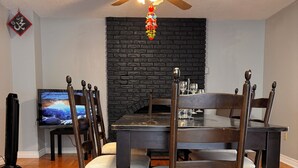 A dining area with a dark wooden table and chairs, a black brick fireplace, a ceiling fan, and a television on the left. - A min walk to the zoo and University!2 bed apartment (Peterborough)