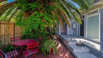 A patio with a red table and chairs, surrounded by lush greenery and a wooden fence.