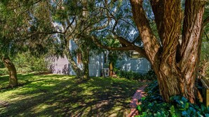 A backyard with a large tree, a lawn, and a house with a garage. - Sea Sounds on Lohr Inverloch (Inverloch)