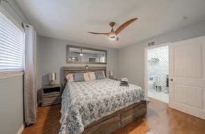 A bedroom with a bed, a ceiling fan, a mirror, a nightstand, and a door leading to a balcony.