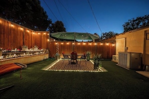 An outdoor patio with a table and chairs, surrounded by a wooden fence, and a small garden area with plants.