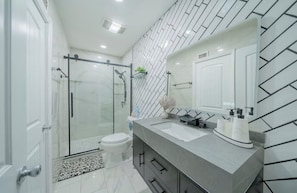 Une salle de bain moderne avec une douche à parois de verre, des toilettes blanches, un meuble-lavabo et un miroir.
