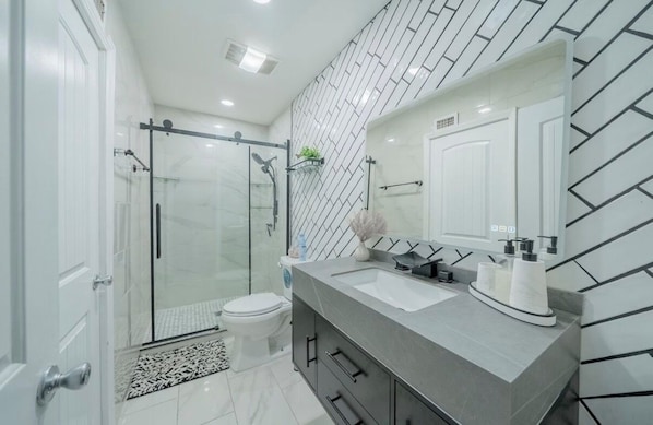 A modern bathroom with a glass shower enclosure, a white toilet, a vanity with a sink, and a mirror.