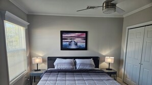 Un dormitorio con cama, dos lámparas de noche, ventilador de techo, un cuadro en la pared y una ventana con persianas.