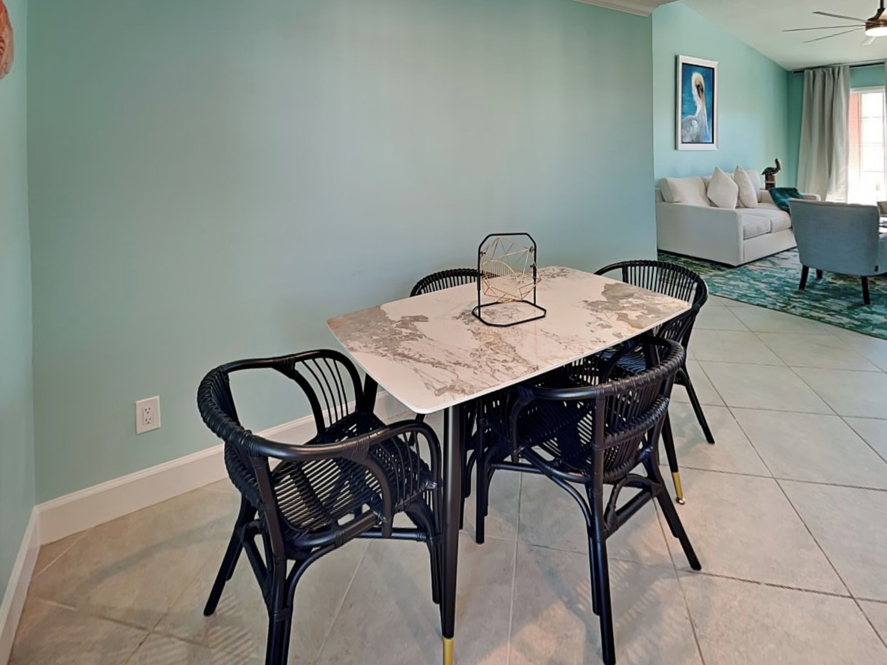 A dining area with a marble table and black wicker chairs, a ceiling fan, and a light blue wall.