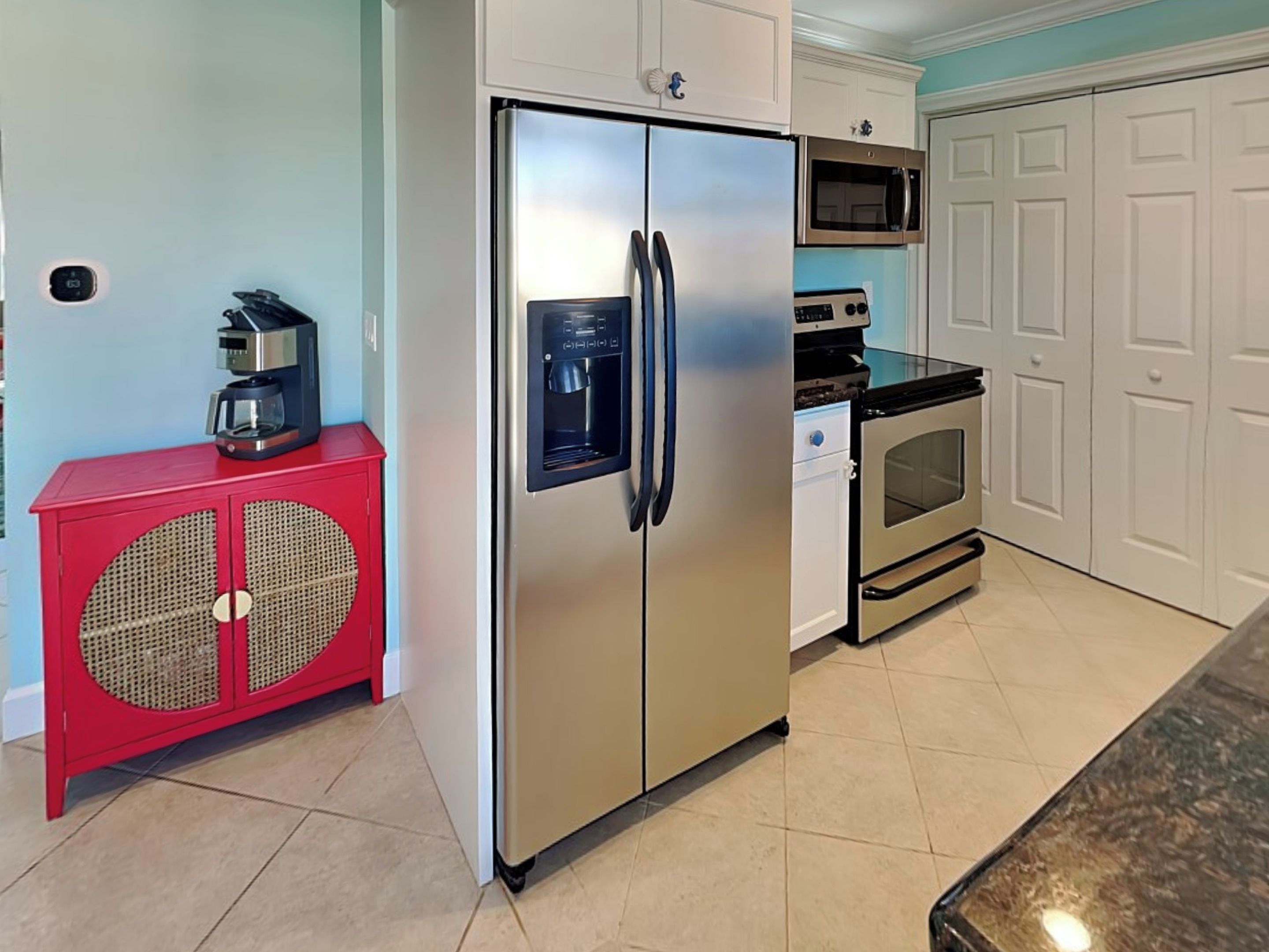 A kitchen with a stainless steel refrigerator, a microwave, a stove, and a red cabinet with a woven front panel.