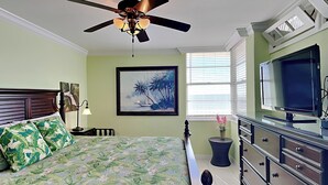A bedroom with a bed, a ceiling fan, a TV, a dresser, and a window with blinds.