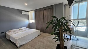 A modern bedroom with a large bed, a potted plant, and a window with a city view. - Central Modern Duplex with Panoramic View (Unknown)