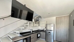 A modern kitchen with a built-in stove, refrigerator, and a flat-screen TV mounted on the wall. - Central Modern Duplex with Panoramic View (Unknown)