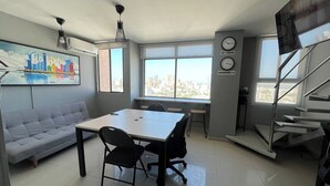 A modern living space with a dining area, a sofa, a staircase, and large windows offering a city view. - Central Modern Duplex with Panoramic View (Unknown)