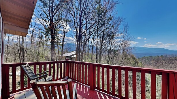 Eine Holzterrasse mit roter Geländer, einem Tisch und zwei Stühlen mit Blick auf eine Berglandschaft.