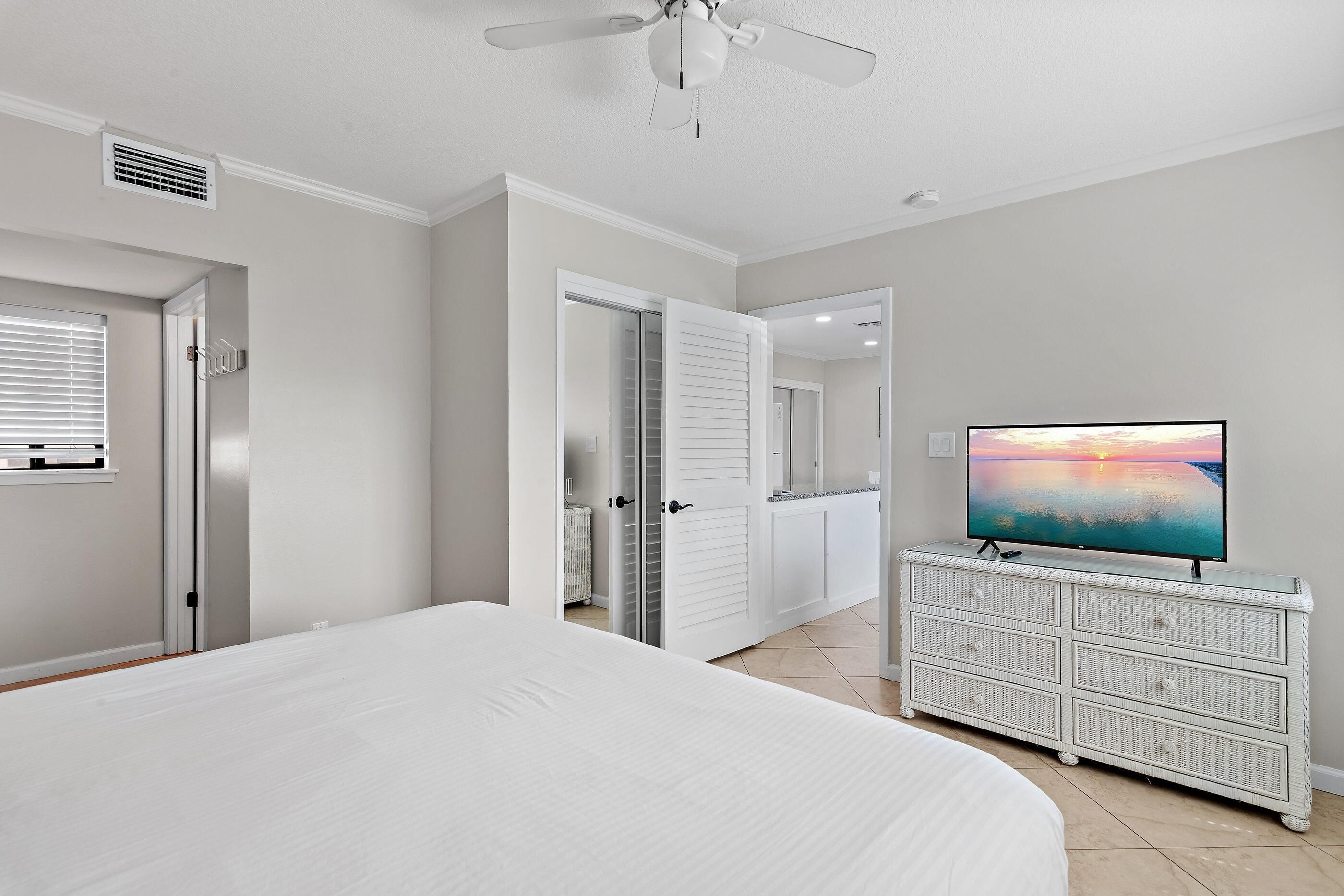 A bedroom with a bed, a dresser, a television, and a ceiling fan.