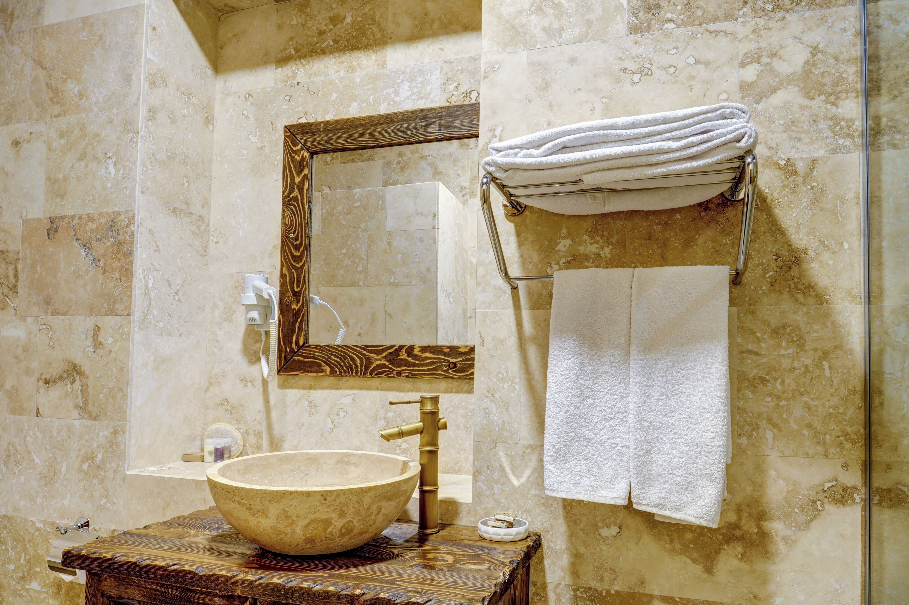 A bathroom with a wooden vanity, a large bowl sink, a mirror with a wooden frame, and a towel rack with towels.