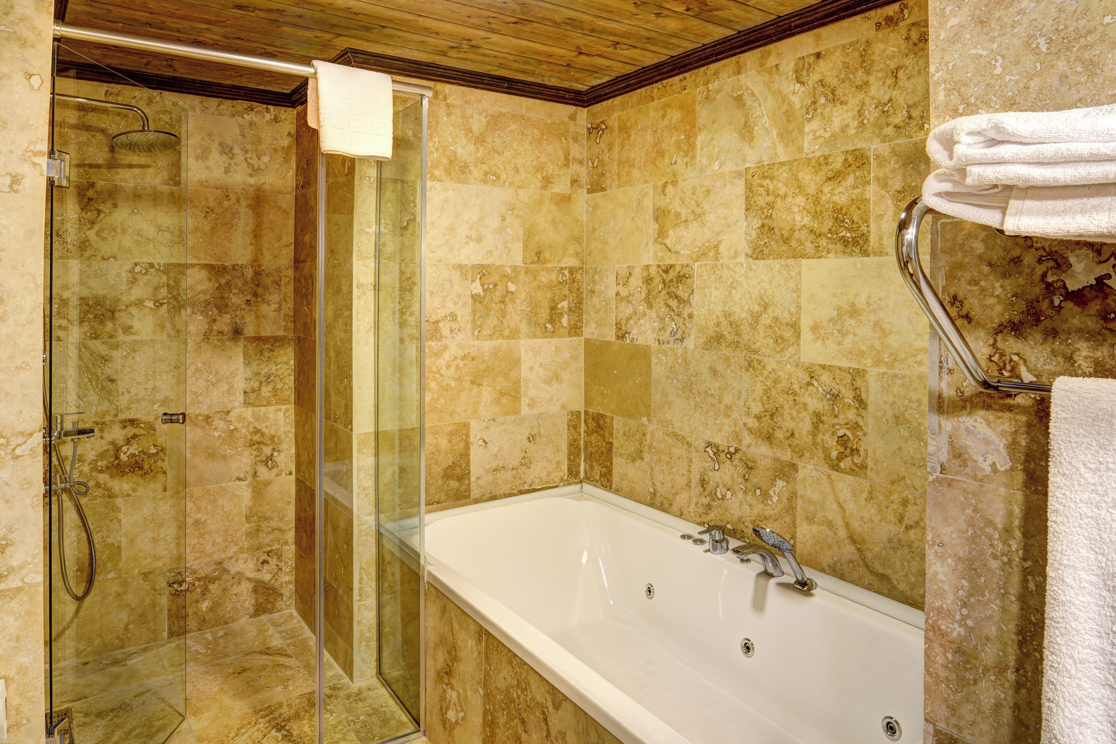 A bathroom with a glass-enclosed shower, a large bathtub, and beige tiled walls.
