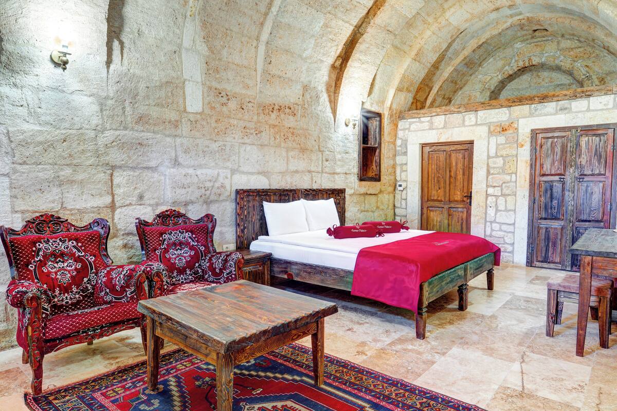 Habitación con paredes de piedra, una cama, muebles de madera y una alfombra estampada.