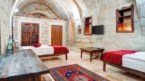 A room with two beds, a wooden table, a TV, and stone walls.