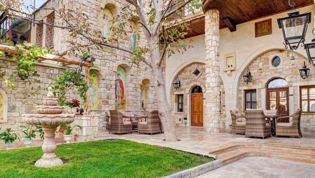 A courtyard with stone walls, a fountain, wicker furniture, and a wooden ceiling.
