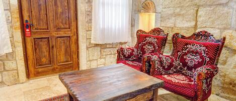 Una habitación con puerta de madera, un banco, dos sillas rojas ornamentadas y una alfombra estampada.