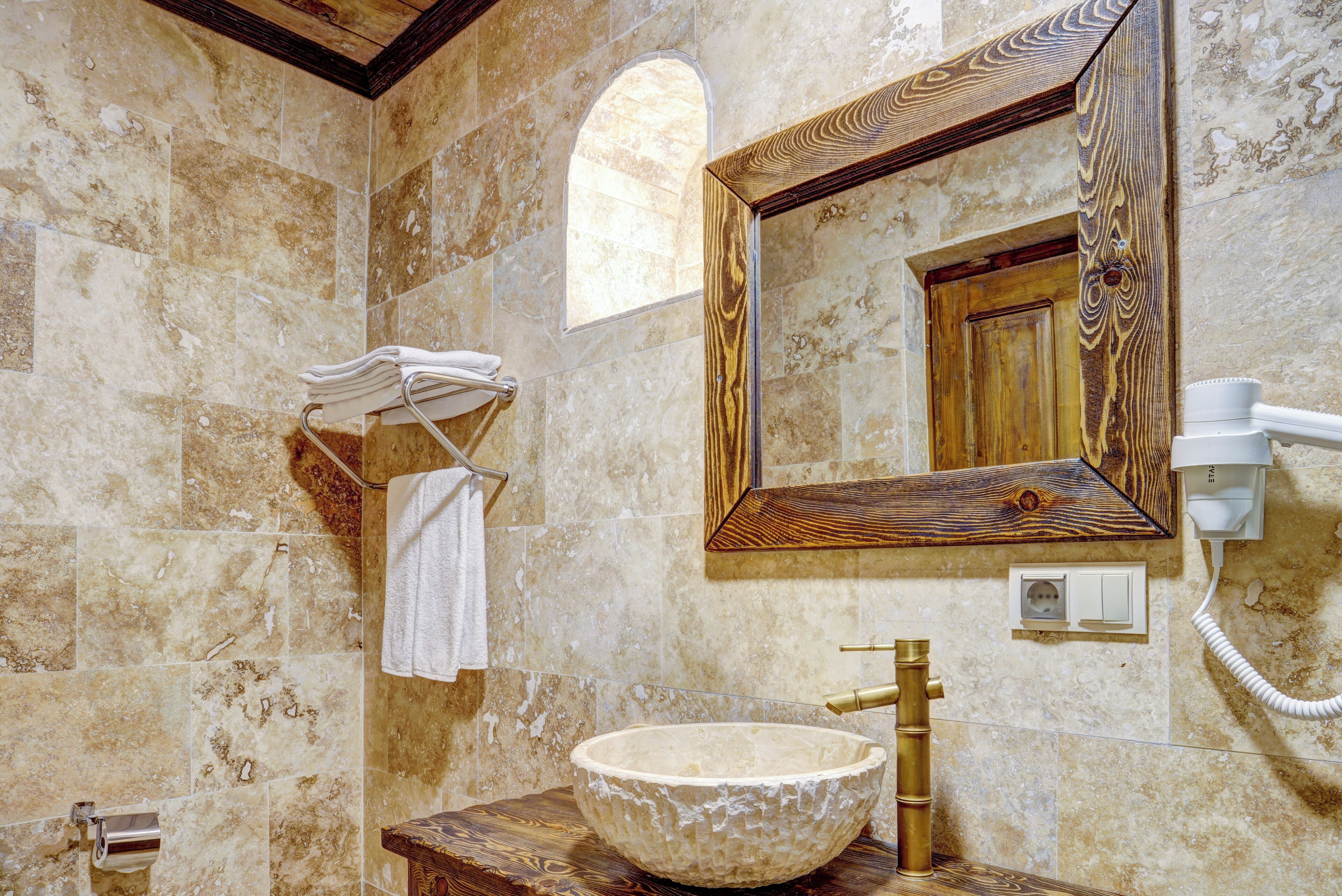 A bathroom with a large stone sink, wooden vanity, a towel rack, and a mirror with a wooden frame.