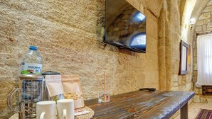 A rustic stone wall with a wooden table set with a water bottle, a thermos, and two white mugs.