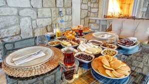 A table set with various breakfast items including bread, pastries, cheeses, and fruits, with a fireplace in the background.
