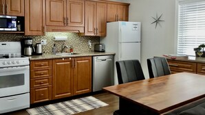 Une cuisine avec des meubles de rangement en bois, un réfrigérateur blanc, une cuisinière et une table à manger avec des chaises.