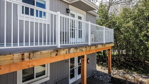 Une maison grise avec une terrasse en bois et des balustrades blanches.