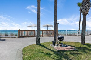 Un camino pavimentado que conduce a una zona de playa con palmeras, una parrilla y sombrillas.
