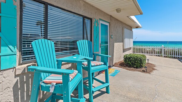 Een accommodatie aan het strand met turquoise stoelen en een tafel, een wit hek en uitzicht op de oceaan.