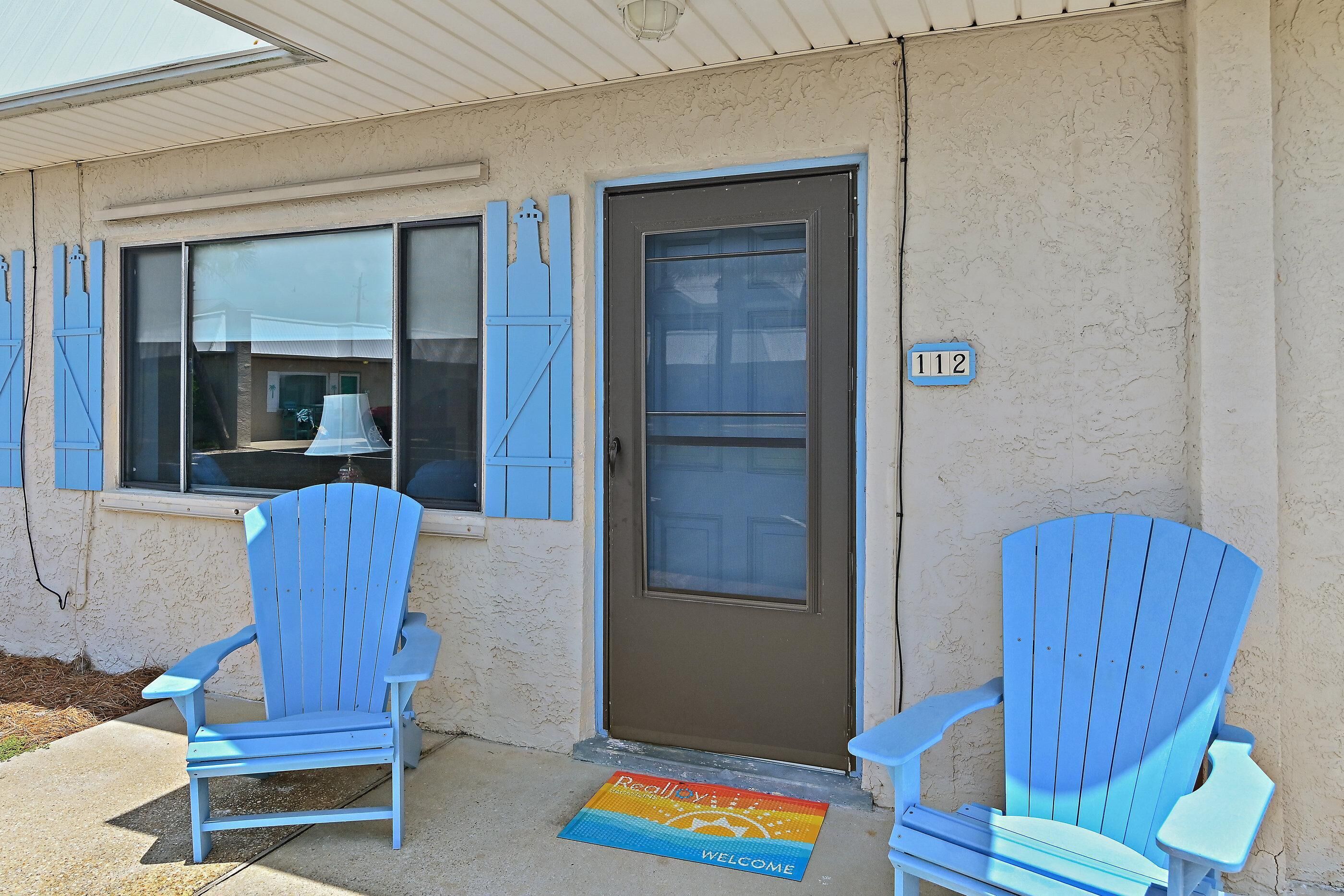 A building with a brown door and two blue Adirondack chairs outside.