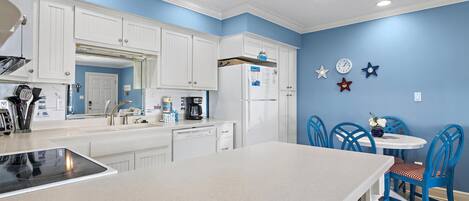 A kitchen with white cabinets, a central island, and a dining area with blue chairs.
