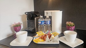 Ontbijt in een hotelkamer, met koffiezetapparaat, twee waterflesjes, een theeset en twee potplanten.