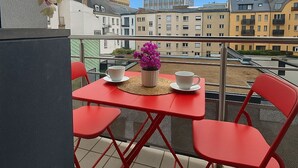 Een balkon met rode stoelen en een tafel, een plant in pot en uitzicht op gebouwen.
