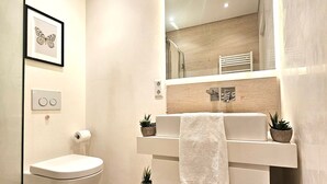 Een moderne badkamer met toilet, wastafel en spiegel. Er staan potplanten op het aanrecht en een handdoek hangt aan de muur.
