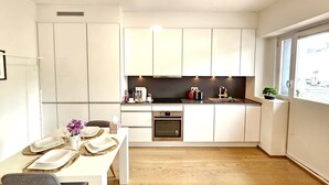 Een moderne keuken met witte kasten, een eethoek met een tafel voor twee en een raam dat voor natuurlijk licht zorgt.