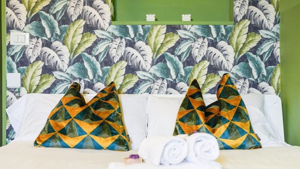 A hotel room with a bed, two patterned pillows, and rolled towels on the bed.