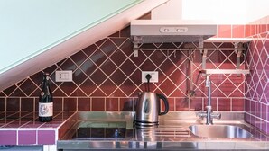 A kitchen with a microwave, kettle, and stainless steel sink.
