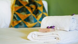A neatly folded white towel with a soap bar and a purple flower on a bed.