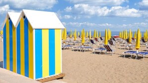 Une plage avec des cabanes de plage rayées et des rangées de chaises longues sous des parasols jaunes.