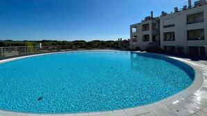Une grande piscine aux eaux cristallines, entourée d’un bâtiment moderne doté de balcons.