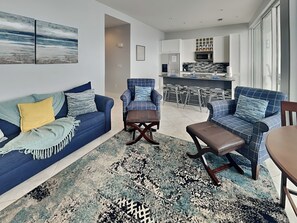 A modern living room with a blue sofa, a blue armchair, and a patterned rug.