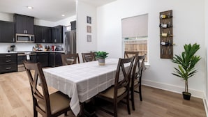 Una cucina moderna con mobili scuri, un forno a microonde e una zona pranzo con tavolo e sedie. Si nota una pianta in vaso e una cantina a parete.