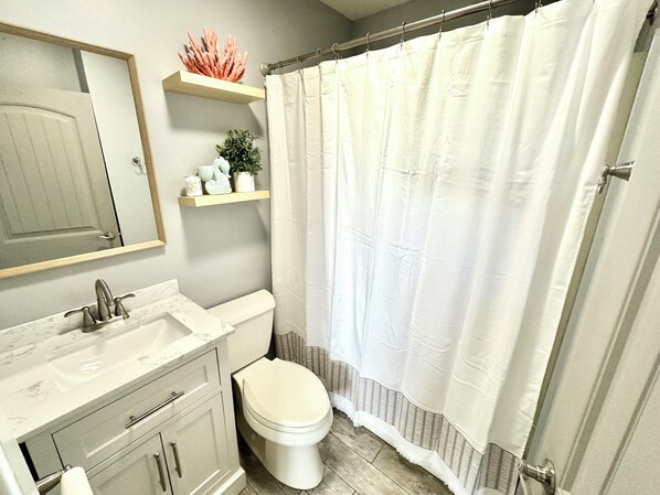 A bathroom with a toilet, sink, and mirror. There are shelves above the mirror and a shower curtain.
