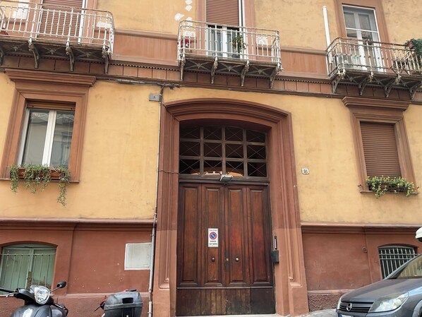 A building with a wooden door, a balcony with railings, and a window with a plant.