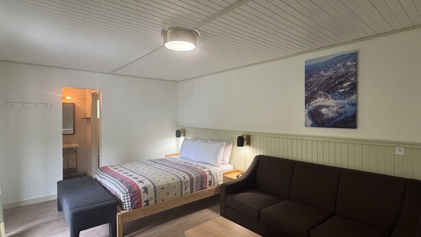 A bedroom with a bed, a sofa, a bench, a bedside table, and a nightstand. - Queen Room With Balcony - NQB (Gatlinburg)