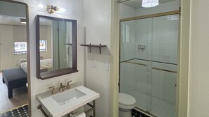 A bathroom with a white sink, a mirror, a towel rack, a shower with glass doors, and a black and white tiled floor. - Queen Room With Balcony - NQB (Gatlinburg)