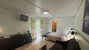 A room with a bed, a sofa, a wooden table, a TV mounted on the wall, and a window with curtains. - Queen Room With Balcony - NQB (Gatlinburg)