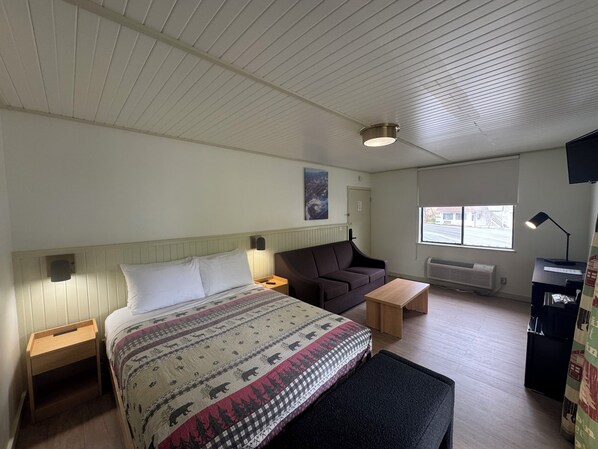 Ein Hotelzimmer mit Bett, Schreibtisch, Stuhl, Bank, Fernseher und Fenster.
