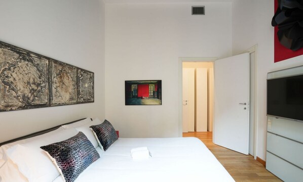 Een slaapkamer met een groot bed, een televisie en een deur naar een andere kamer.