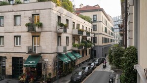 A street view of a building with multiple balconies, a flower shop on the ground floor, and parked cars along the street. - Milan Center | Garibaldi Center Apartment (Milano)